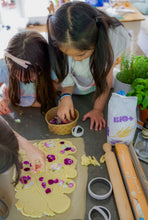 Load image into Gallery viewer, Children making cookies with floral decorations on a kitchen counter.