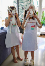 Load image into Gallery viewer, Two children holding toy animals over their faces in a room with large windows.