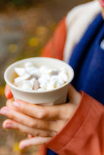 Load image into Gallery viewer, Person holding a cup of hot chocolate with whipped cream outdoors