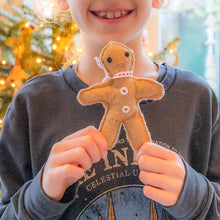Load image into Gallery viewer, Child holding a small gingerbread man ornament with a blurred Christmas tree in the background