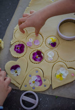 Load image into Gallery viewer, Heart-shaped cookies with flower toppings on a baking sheet.
