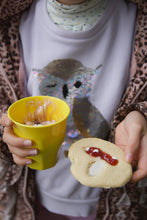 Load image into Gallery viewer, Person holding a yellow cup and a cookie with jam, taken during a Moozlehome kids sewing and cooking workshop
